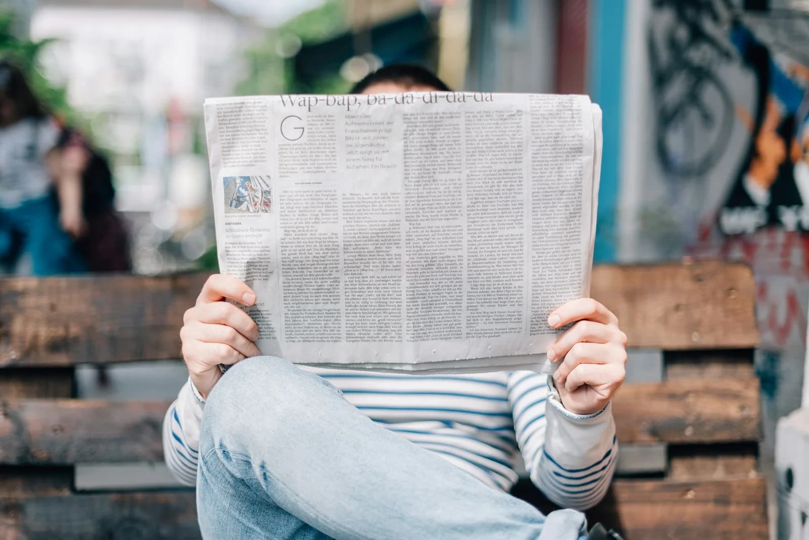 En person sitter på en benk og leser en avis