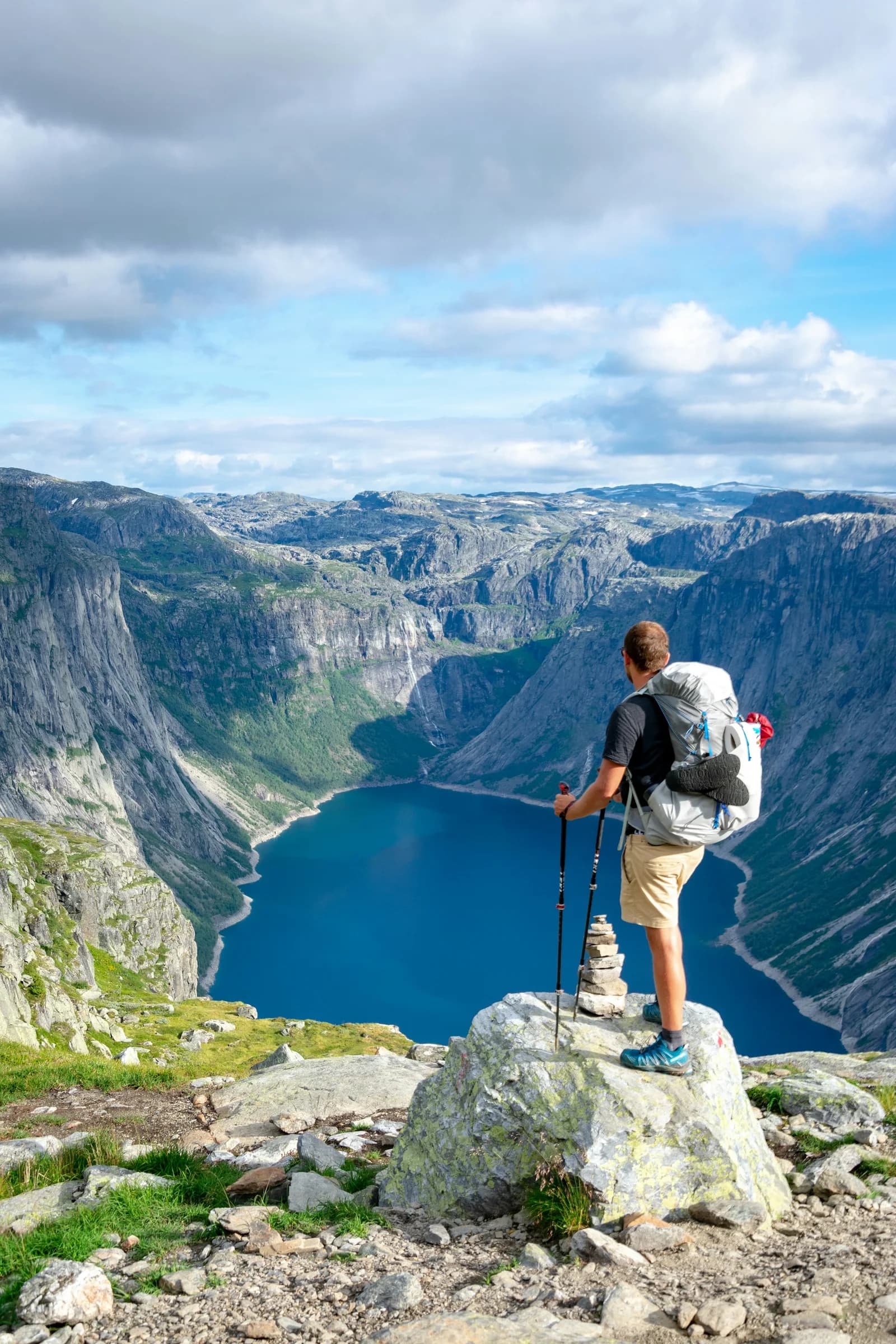 En turgåer med sekk og staver ser utover en fjellinnsjø