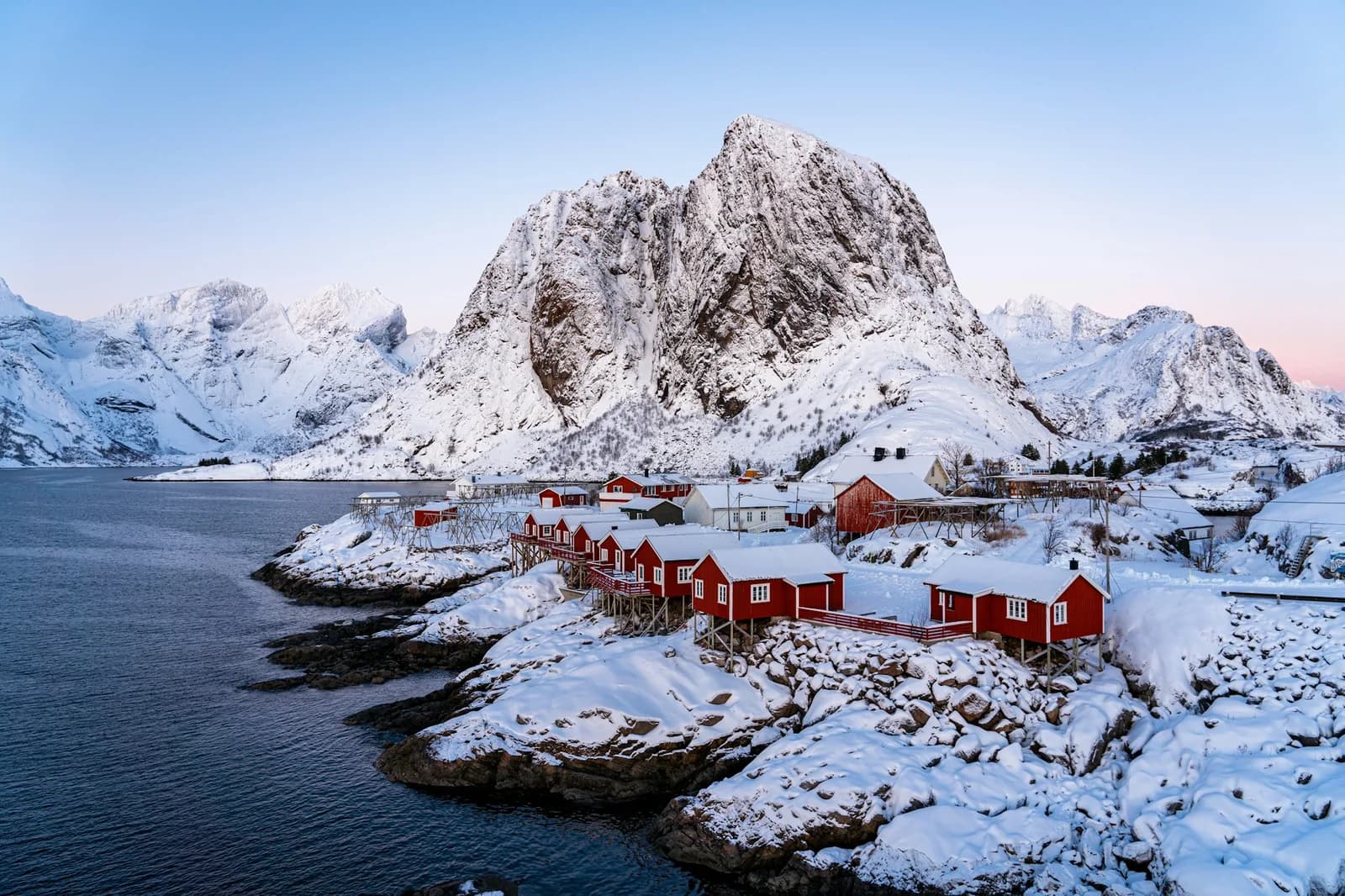 Røde rorbuer ved vannet og snødekte fjell i Lofoten